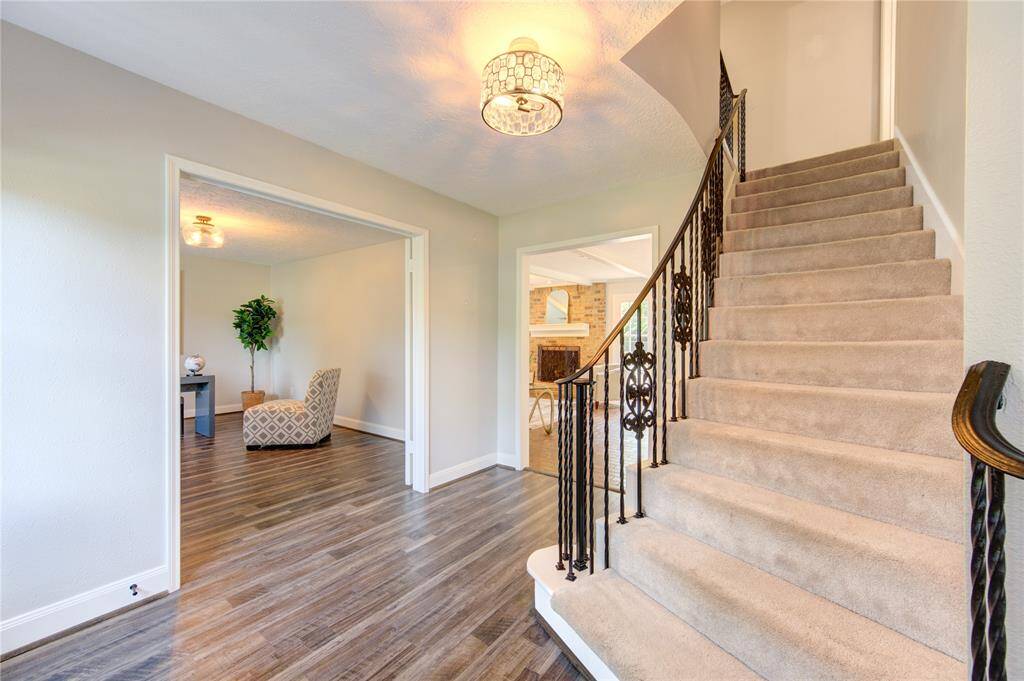 This inviting entryway features stylish wood flooring and a carpeted staircase with ornate railing. It opens to a well-lit room with modern decor and a cozy view of the living area with a fireplace.