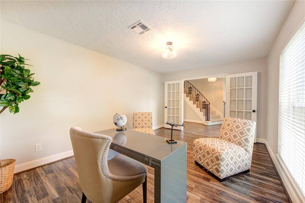 This photo showcases a bright, modern office space with wood floors, a sleek desk, and stylish chairs. French doors open to a view of a staircase, adding to the room's open feel. Large windows provide ample natural light.