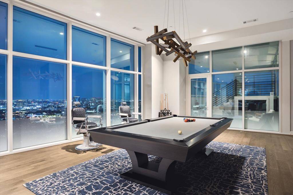Entertain in style with a sleek pool table set against a backdrop of breathtaking panoramic city views in this modern living room.