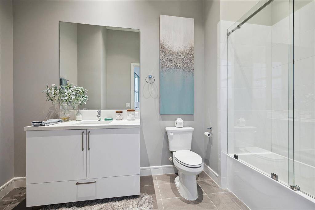 Chic guest bath with sleek vanity and modern glass-enclosed tub.