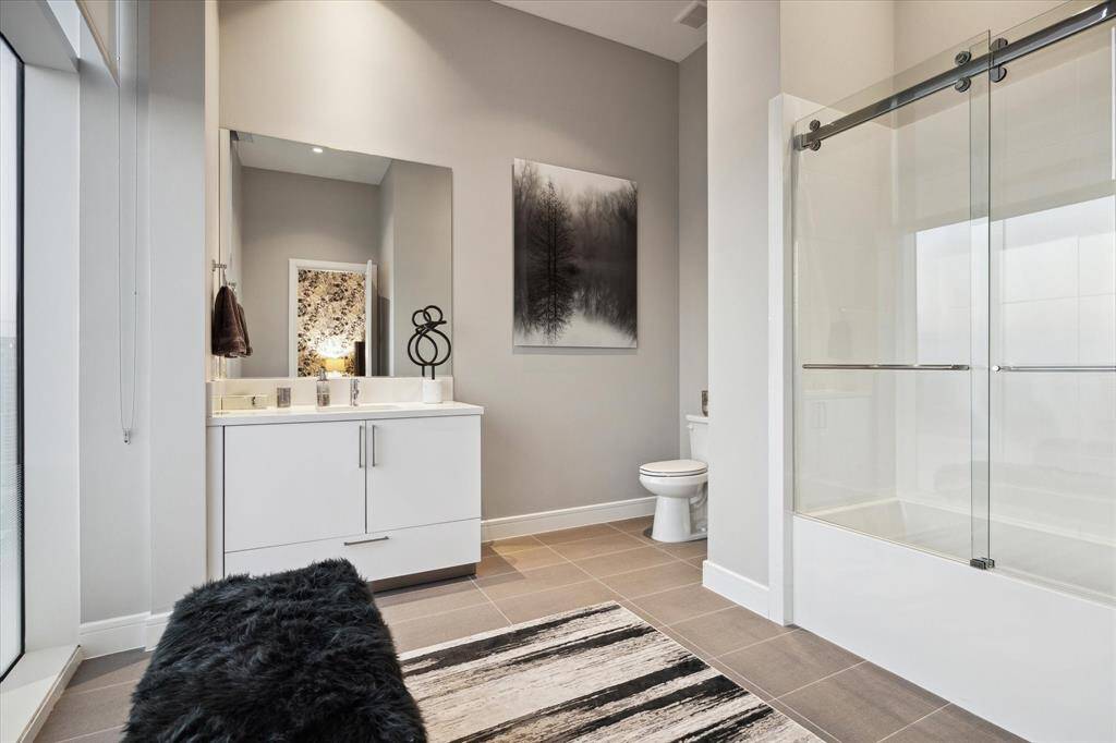 Stylist guest bath featuring a sleek vanity, seating and glass-enclosed soaking tub.