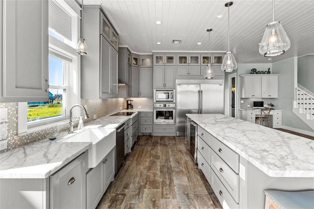 Featuring gray cabinetry, marble countertops, stainless steel appliances, and elegant pendant lighting. Abundant natural light with coastal-inspired color palette.