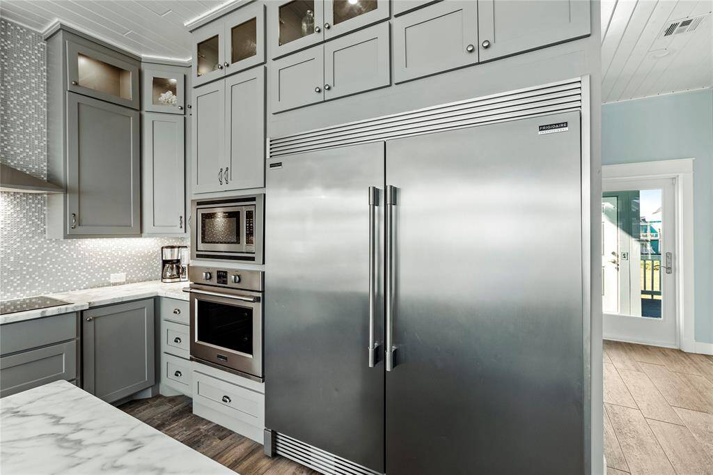 Stainless steel appliances, including a double-door refrigerator and built-in oven and microwave. Elegant gray cabinetry and mosaic backsplash complement the sleek marble countertops.