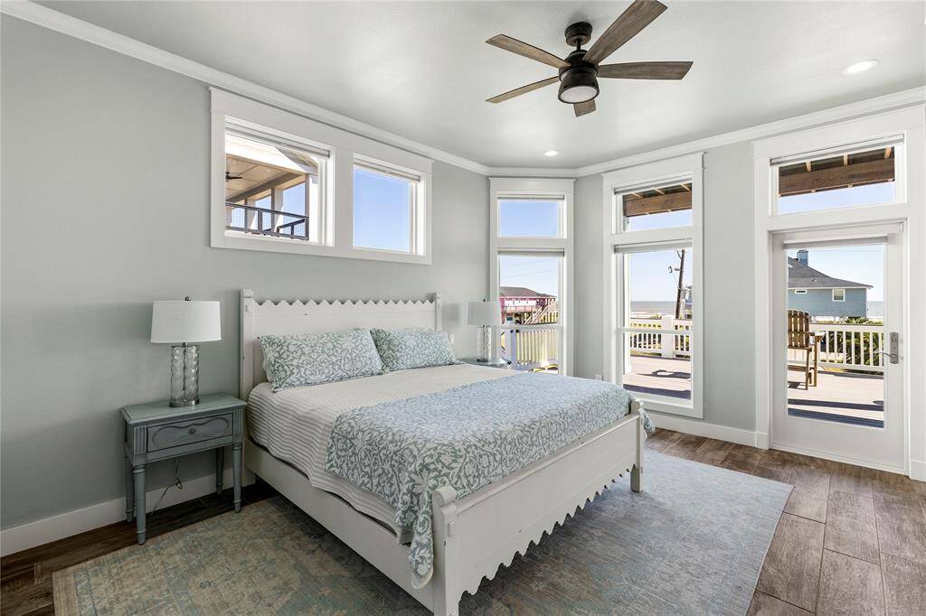 Bright and airy master bedroom suite with wood-look luxury vinyl floors, private bath, large windows offering plenty of natural light, and direct access to a spacious balcony with outdoor seating and ocean views. Features include a ceiling fan and a serene color palette.