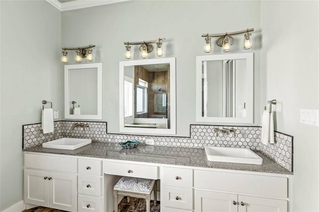 Well-lit double vanity private master bathroom with stylish hexagonal tile backsplash, granite countertops, and modern fixtures.