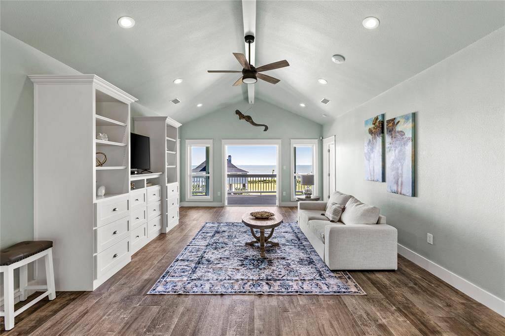 2nd floor living area with high vaulted ceilings with recessed LED lighting, a built-in entertainment unit, and access to a balcony with a beach view.