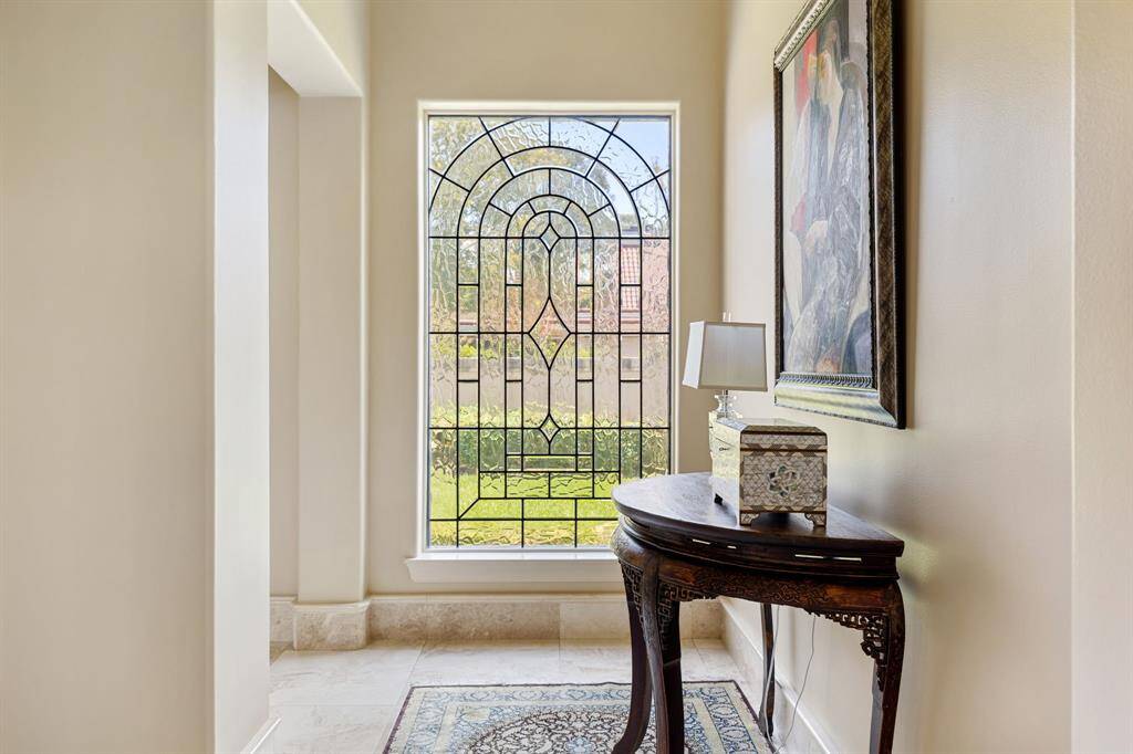 [Library - Level Two] Just when you think you have seen it all—spy a hidden, iron railed spiral staircase that leads the Second Floor of the Library. Surrounding the ellipsis are built-ins and glass display shelves. Through the glass paned French doors is a Juliet balcony overlooking oak shaded Sturbridge Drive. Behind us are double doors with a vista of the second level and the Grand Foyer beyond.