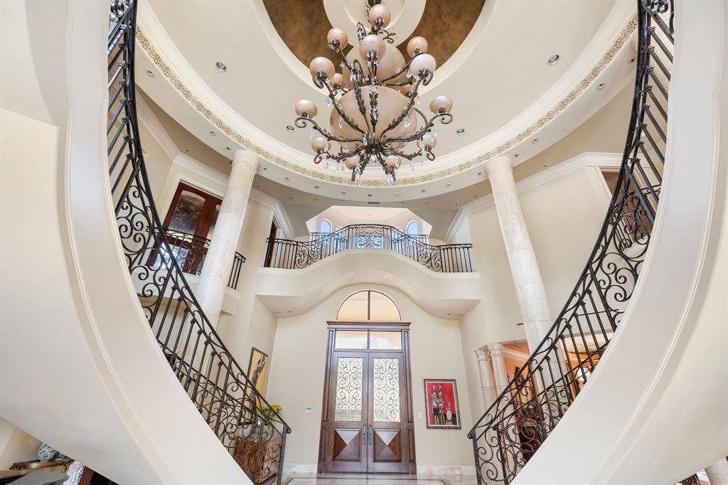 [Grand Foyer] Forming the heart of the home, the Grand Foyer is palatial in scale with a captivating double marble clad helical staircase, Baroque round stone columns, and Marble floors with decorative inlays. The light within is boundless!