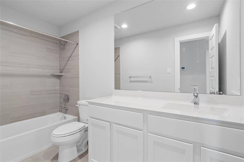 Secondary bath features tile flooring, bath/shower combo with tile surround, stained cabinets, beautiful light countertops, mirror, sleek fixtures and modern finishes.