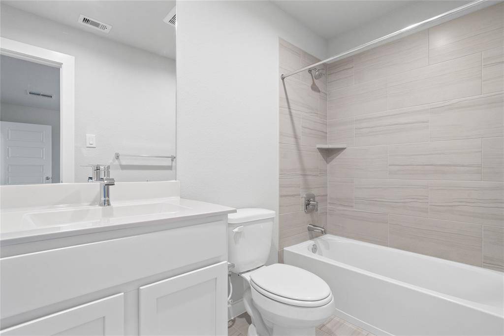 Secondary bath features tile flooring, bath/shower combo with tile surround, stained cabinets, beautiful light countertops, mirror, sleek fixtures and modern finishes.