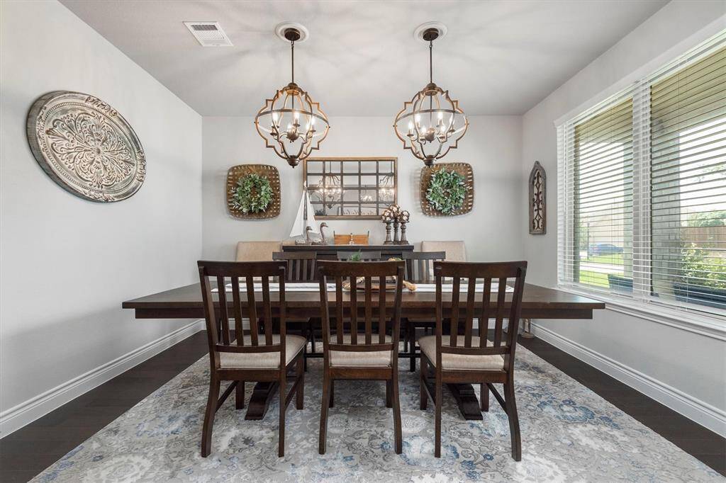Elegant dining room with wooden table and chairs, ornate metal light fixtures, decorative wall art, and a large window with blinds.