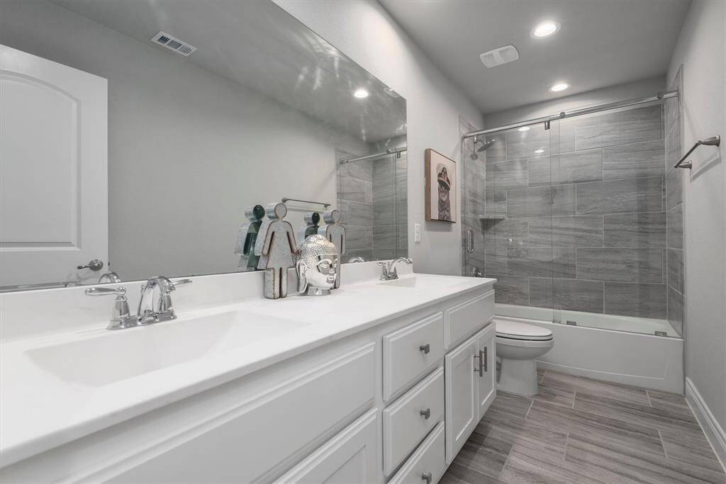 Guest bathroom located across media room has lots of cabinets for storage with an added glass shower doors.