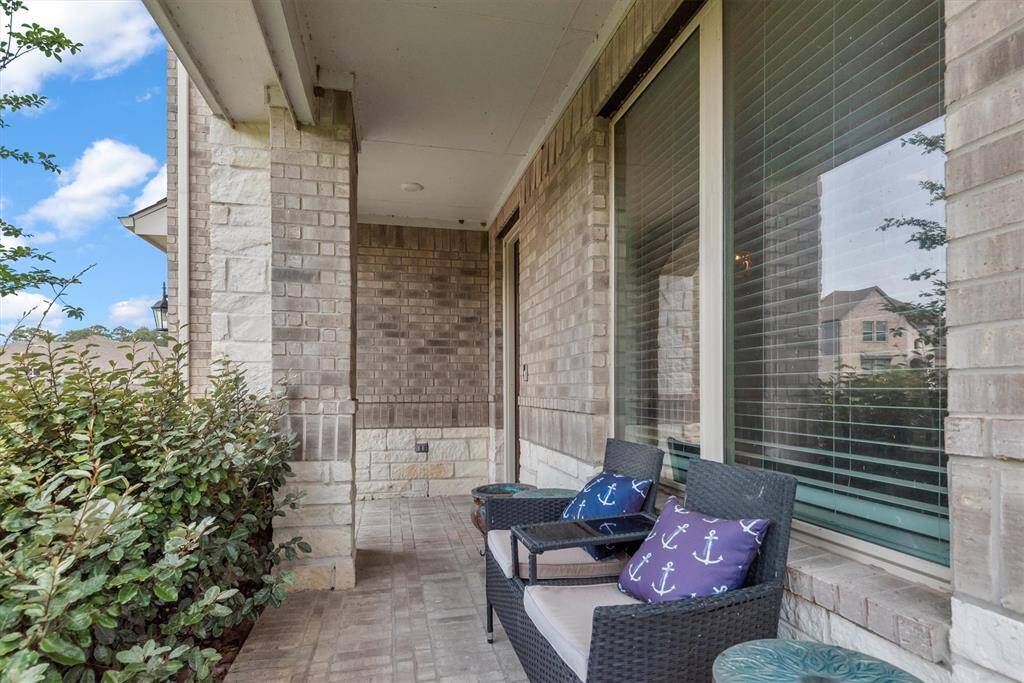 Large porch with comfy chairs and cushions, surrounded by lush greenery and elegant stonework, perfect for a serene and cozy evening.