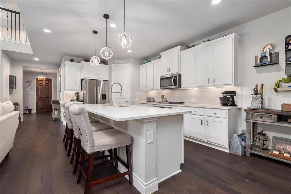 This kitchen is perfect for entertaining guests with its huge island and open layout into the family room, featuring white cabinetry and modern lighting.
