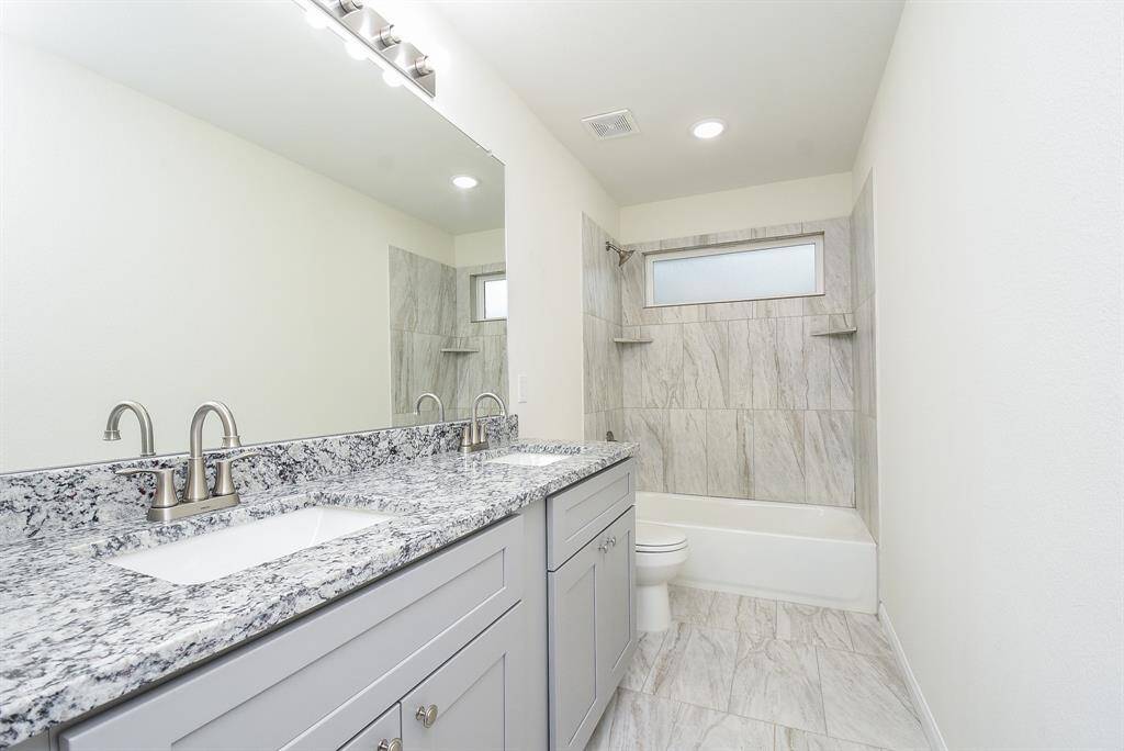 Modern bathroom with double vanity, large mirror, marble tiles, and a bathtub. Clean, bright, and unoccupied.