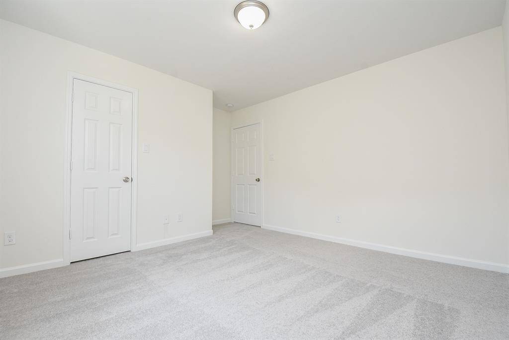 This is a spacious, well-lit room with neutral walls and carpeting, featuring a ceiling light fixture and two doors, offering a clean canvas for personalization.