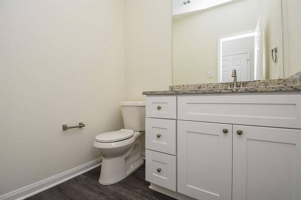 A clean, modern bathroom with a white toilet, vanity cabinet, granite countertop, and a mirror reflecting a doorway.