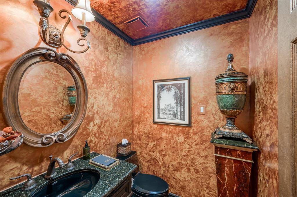 The half bathroom, positioned just off the foyer, boasts a bronze Jado faucet, Kohler undermount sink and toilet, granite countertops, hardwood flooring, and French plaster gold paint from Italy.