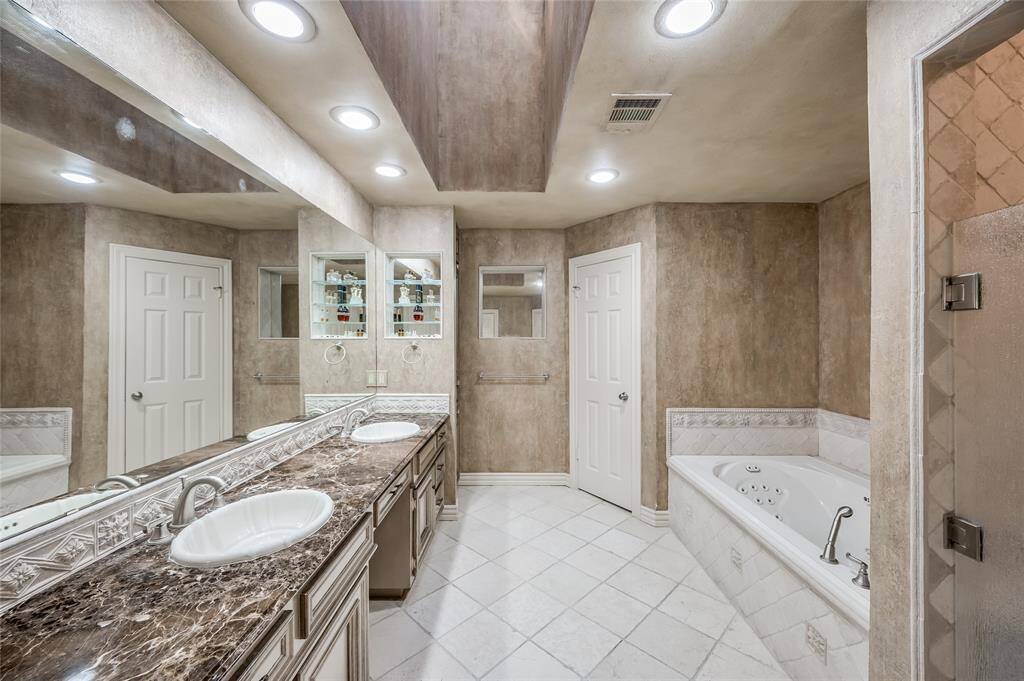 The primary bathroom offers a double vanity with marble countertops, a jacuzzi tub, and a walk-in shower with privacy glass, all set against imported Italian tumbled marble.