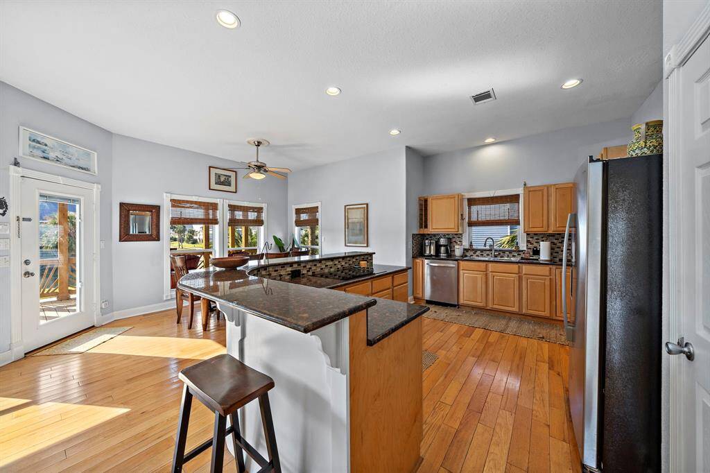 This angle showcases the generous kitchen layout, bar seating, and easy access to the outdoor deck. The flow between the kitchen, dining, and living areas makes for seamless indoor-outdoor living.