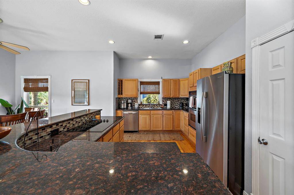 This bright and functional kitchen features natural wood cabinetry, dark granite countertops, and a sleek tile backsplash. A large window over the sink fills the space with natural light and offers views of the lush greenery outside.
