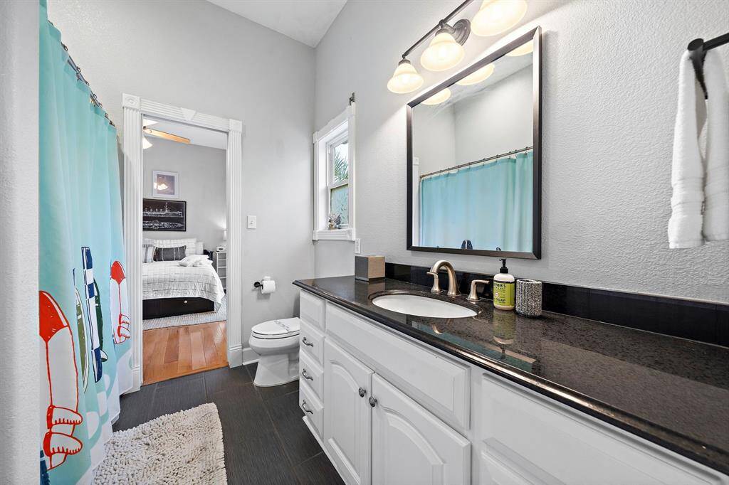 This full bathroom connects two guest bedrooms and features a sleek black granite countertop, bright white cabinetry, and playful shower curtain with coastal charm.