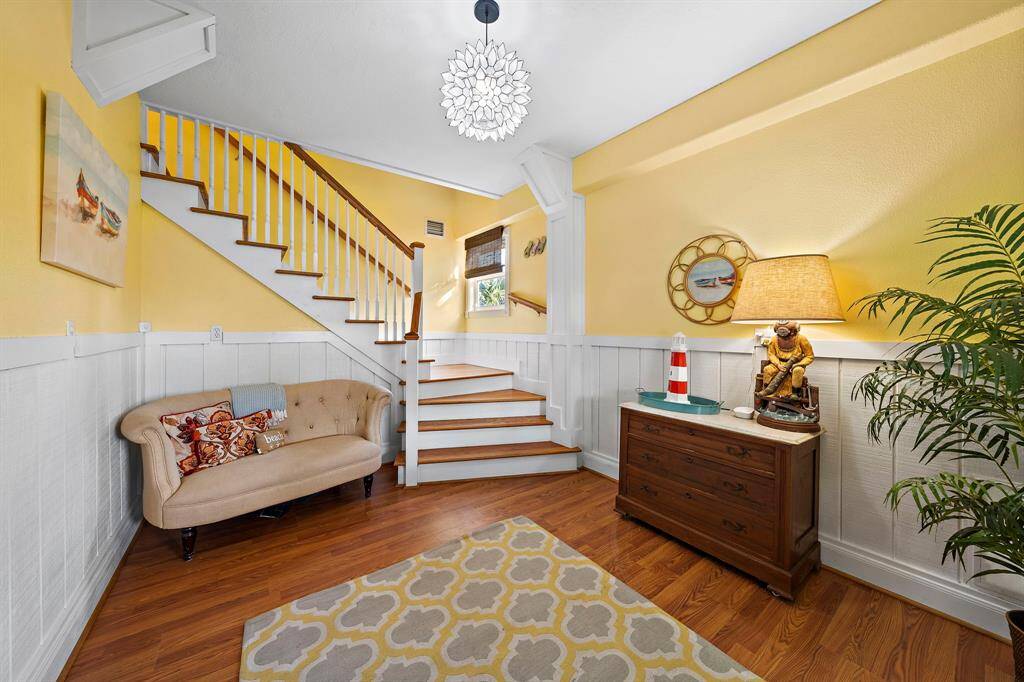A cheerful, coastal-inspired entryway welcomes you with warm yellow walls, wainscoting detail, and an inviting seating nook. The stairway leads to the main living area, setting the tone for the home’s beachy charm.