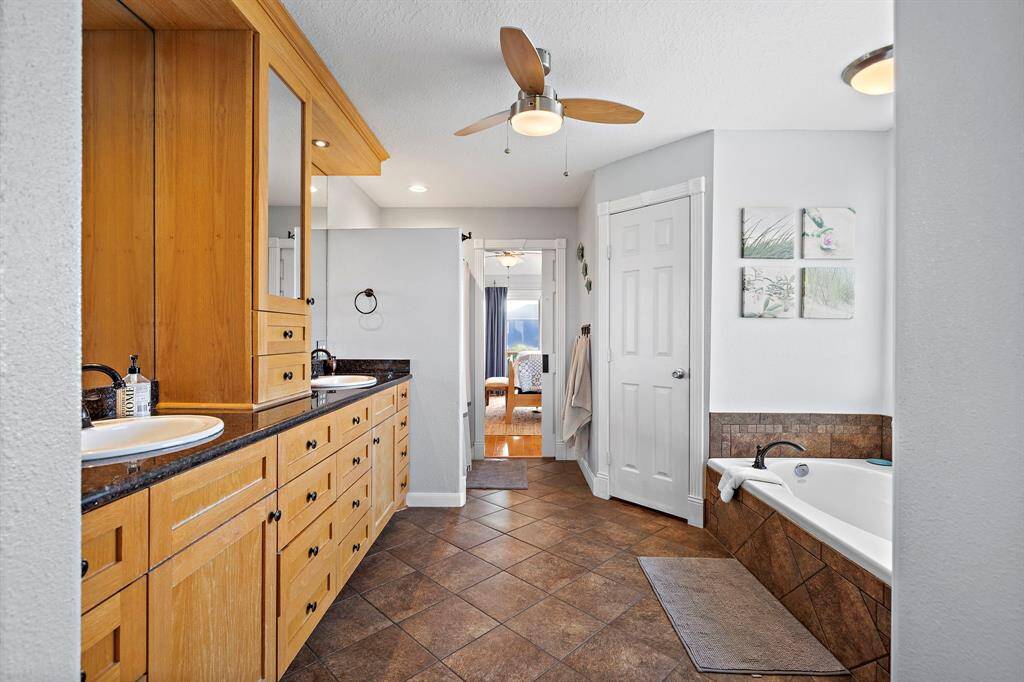 A view from the tub area reveals the layout of the bathroom, including the double vanity. Neutral tile floors and a ceiling fan add to the comfort.