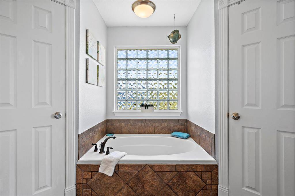 Relax and unwind in the large soaking tub, framed by earthy-toned tile and a glass block window that fills the space with soft, natural light.