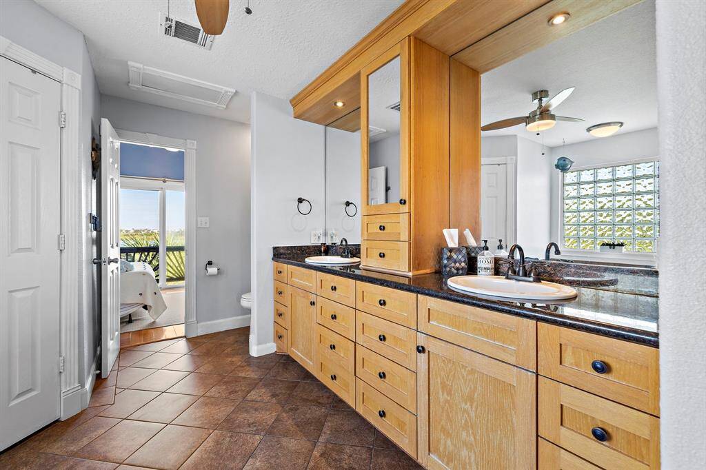 This spacious primary bathroom features dual sinks with abundant counter space, custom wood cabinetry, and a large mirror. Thoughtfully designed with both functionality and style in mind.