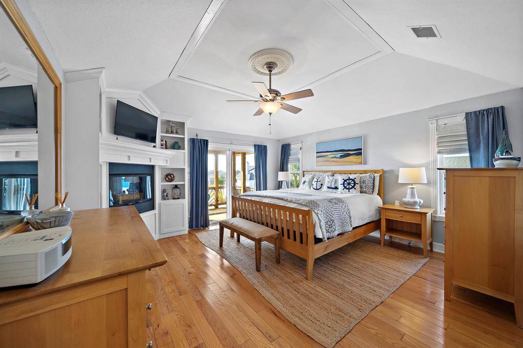 This generously sized primary bedroom showcases coastal charm and functionality, with hardwood floors, dual nightstands, a reading bench, and sliding doors leading to the upper deck for sunrise views.
