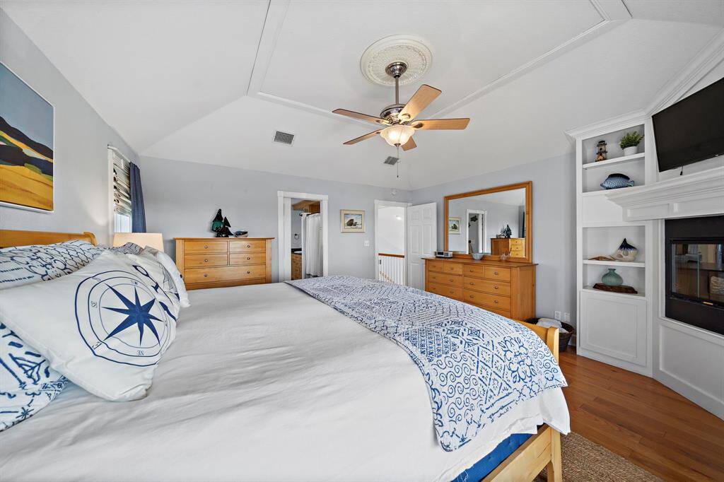 Retreat to a serene primary suite featuring a custom ceiling detail, built-in shelving, a cozy fireplace, and access to the upper deck. Natural light fills the space, creating a peaceful, airy ambiance.
