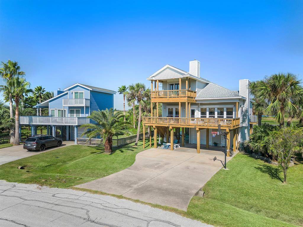 Surrounded by tropical landscaping, this beautiful coastal home features expansive decks, covered parking, and a wide driveway. The warm wood tones and classic coastal style give this home standout curb appeal.