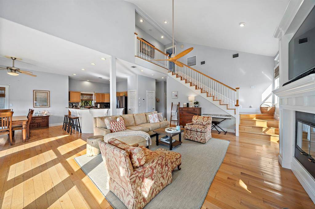 The spacious living room is anchored by a large sectional and inviting accent chairs, with a direct line of sight into the kitchen and dining space. The open floor plan is bathed in natural light, enhancing the airy feel throughout.