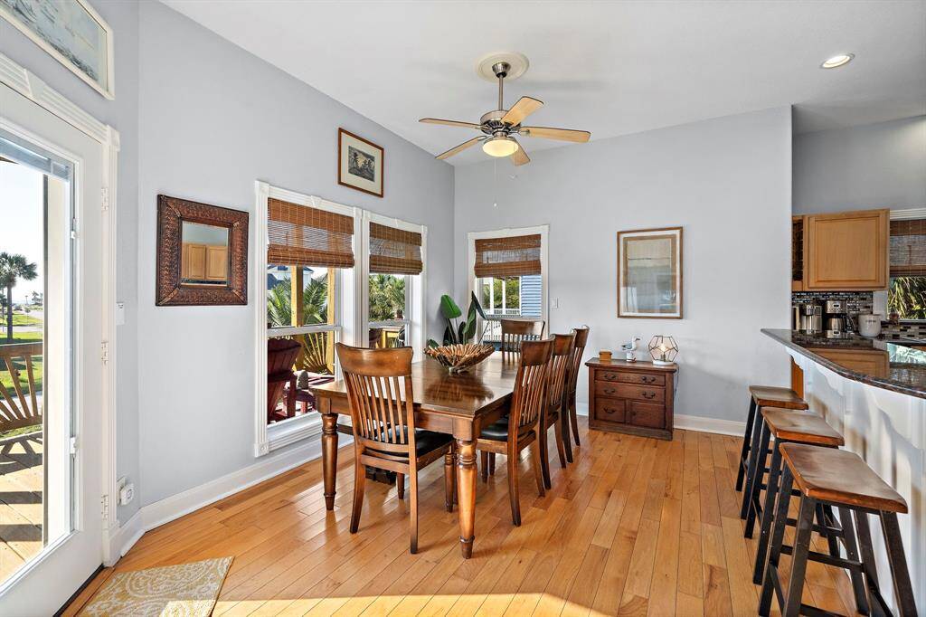 Surrounded by large windows and tropical scenery, the dining space exudes casual coastal elegance. Bamboo shades and classic trim elevate the space while maintaining a relaxed beach-house feel.
