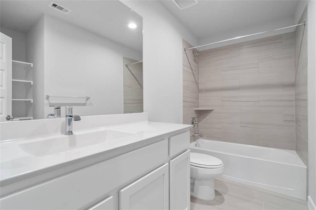 Secondary bath features tile flooring, bath/shower combo with tile surround, stained wood cabinets, beautiful light countertops, mirror, sleek fixtures and modern finishes!