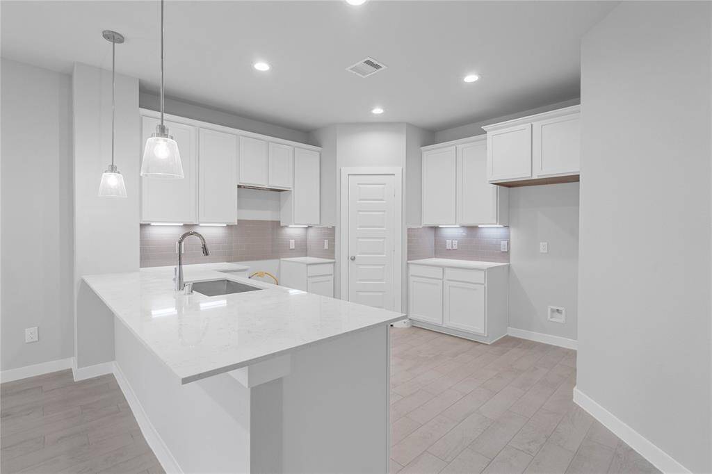 This view of this gorgeous kitchen showcases quartz countertops, beautiful tile backsplash, high ceiling, recessed and pendant lighting, extended countertop for breakfast bar, and wood look tile floors!