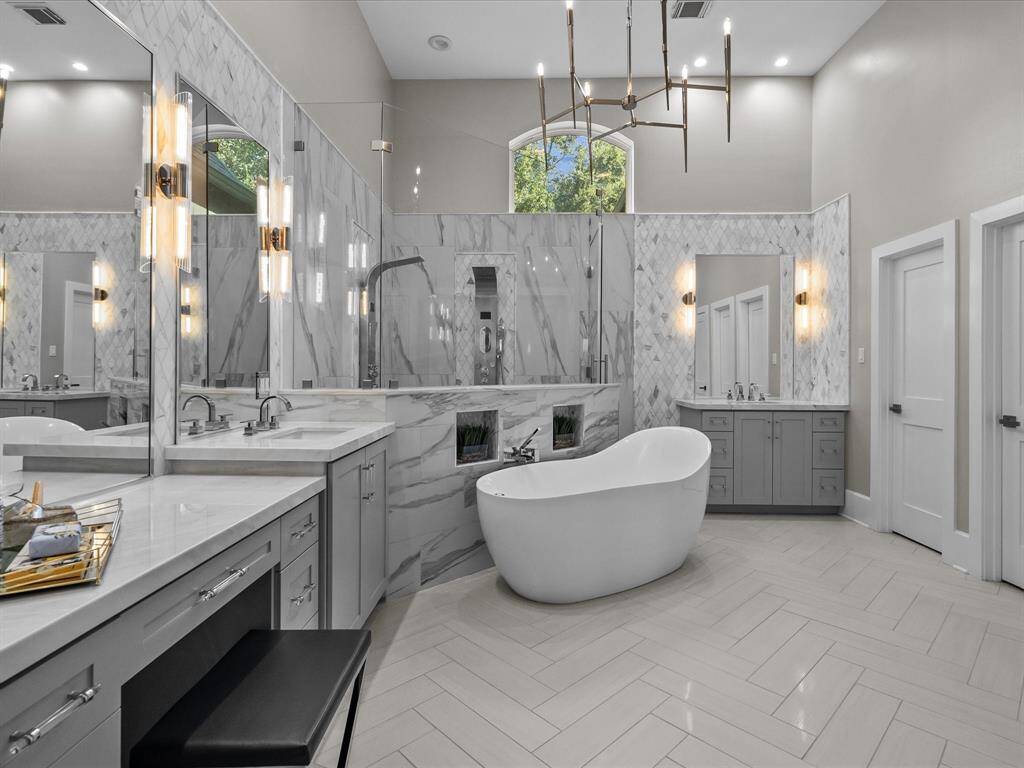 This is a spacious, modern bathroom with elegant finishes, featuring a large freestanding bathtub, dual vanities, stylish lighting fixtures, and a separate shower area.