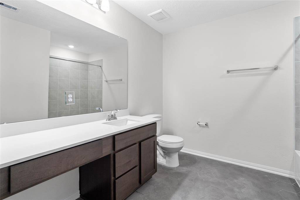 Secondary bath features tile flooring, bath/shower combo with tile surround, wood cabinets, beautiful light countertops, mirror, sleek fixtures and modern finishes!
