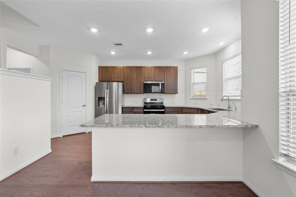 This spacious kitchen features high ceilings, recessed lighting, stained cabinets with granite countertops, SS appliances, modern tile backsplash, extended countertop for breakfast bar, and a walk-in pantry all overlooking your huge family room.