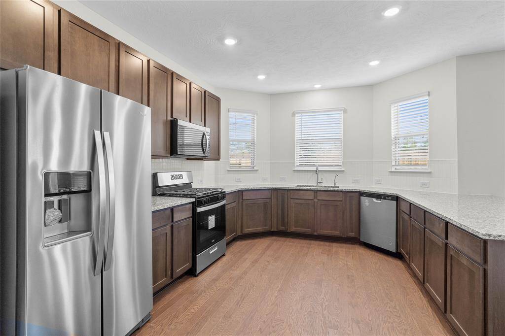 Another view of this spacious kitchen featuring large windows with privacy blinds, high ceilings with recessed lighting, stained cabinets with granite countertops, SS appliances, modern tile backsplash, extended countertop for breakfast bar, and a walk-in pantry all overlooking your huge family room.