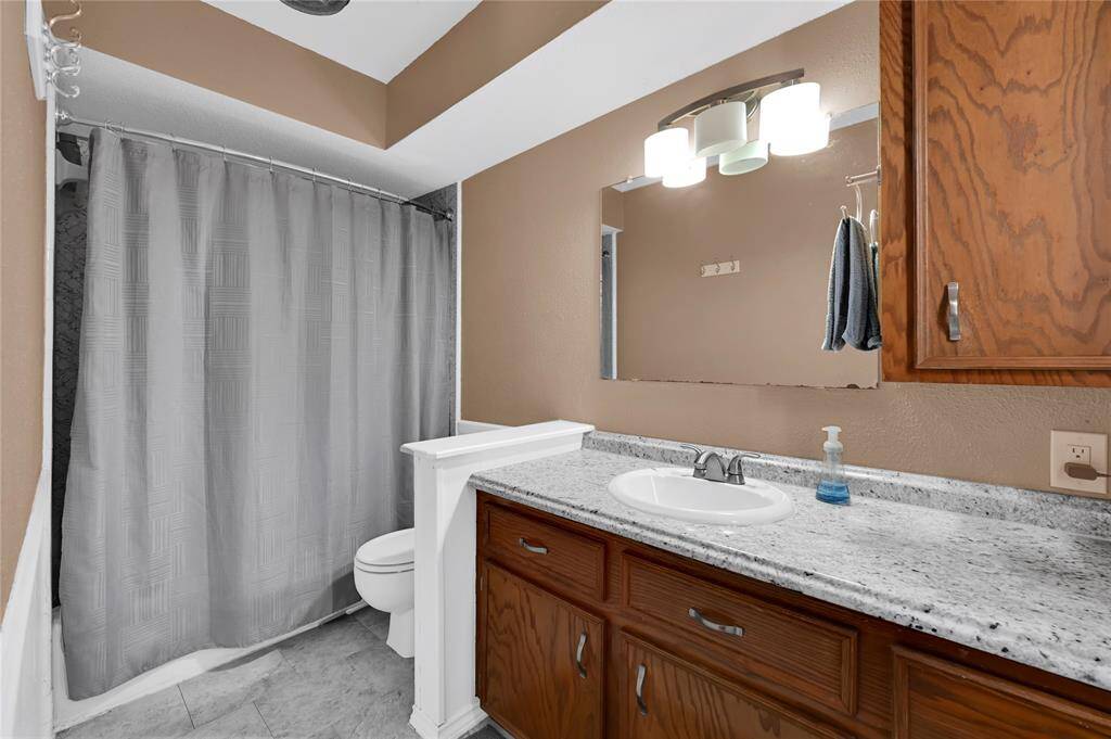 Well-maintained bathroom with a granite countertop, undermount sink, wooden cabinetry, and a full-size tub/shower combination. It features tiled flooring and a neutral color scheme.