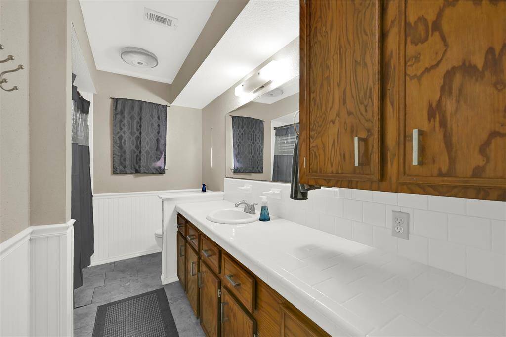 The spacious secondary bathroom featuring a long countertop, traditional wooden cabinetry, mirrors, and complementary tile backsplash.