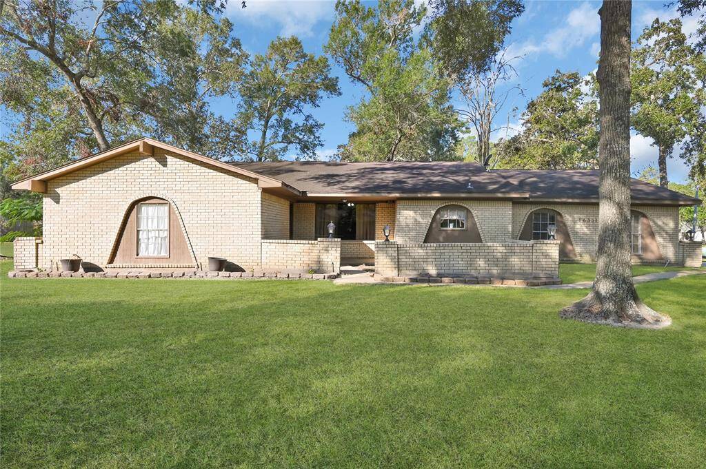 Charming single-story brick home with a spacious front lawn and mature trees, featuring distinctive arched windows and a cozy covered entrance.