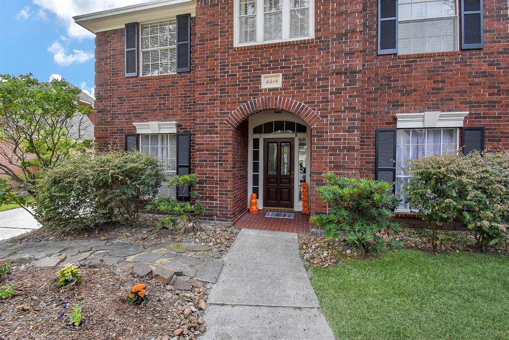 Charming brick home with black shutters, featuring a welcoming arched entryway. The front yard is landscaped with shrubs and flowers, offering a quaint path leading to the door. Perfect curb appeal for buyers seeking a classic look.