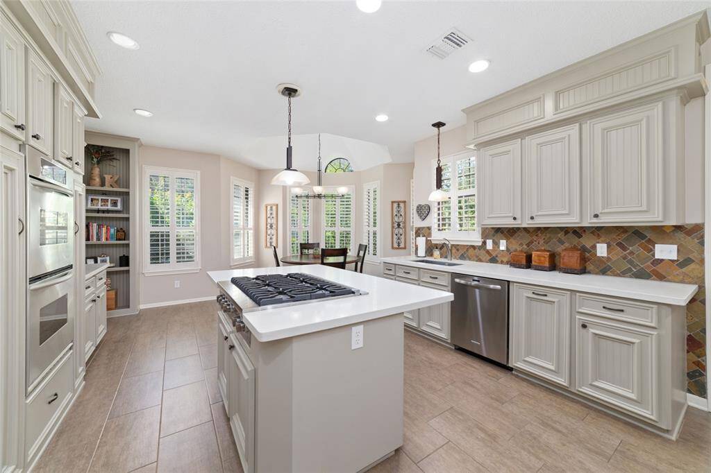 This spacious updated kitchen boasts quartz counters and sleek cabinetry complemented by stainless steel appliances and a central island with a 6 burner gas cooktop with downdraft exhaust. Ample natural light pours in through multiple windows framed with classic plantation shutters, enhancing the bright and open feel of the space.