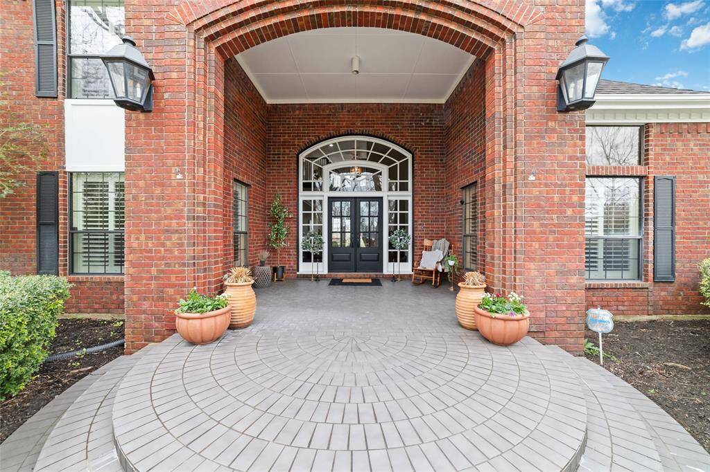 This inviting front entryway exudes charm and elegance, highlighted by a beautiful brick archway and stately double doors, creating a warm, welcoming atmosphere for guests.