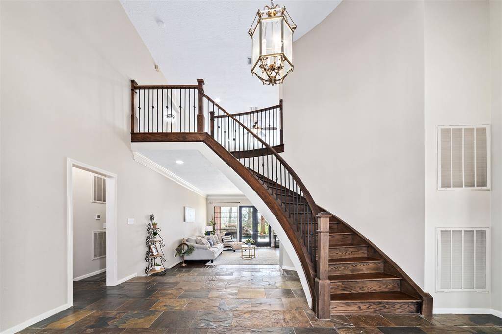 You're greeted by an elegant entryway showcasing a sweeping wooden staircase with intricate iron balusters, gracefully leading to the second-floor landing. The foyer's slate tile flooring adds a modern touch, while the view opens into a bright living space with gleaming hardwood floors. Neutral wall tones and a classic chandelier complete the scene, creating a timeless and sophisticated atmosphere.
