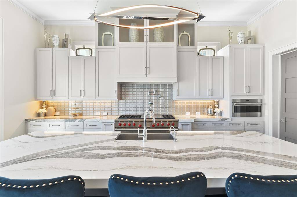 Experience the elegance of custom cabinetry with intricate millwork, illuminated by stunning under and over cabinet lighting. The gorgeous quartz countertops with waterfall edges on the island make this kitchen the centerpiece of modern coastal living.