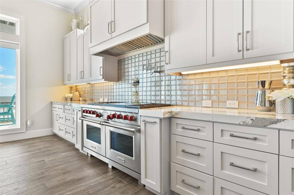 Prepare meals in style with a massive 60" dual fuel Wolf range, stunning custom cabinetry, and a beautiful quartz kitchen island featuring waterfall edges. This kitchen is truly the heart of this luxury beachfront home.
